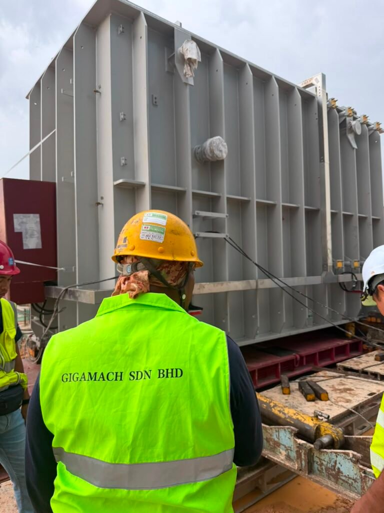 Gigamach team member in high-visibility PPE monitoring a transformer unloading work area.