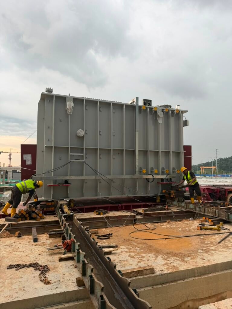 Workers managing support materials during the controlled unloading of a large transformer.