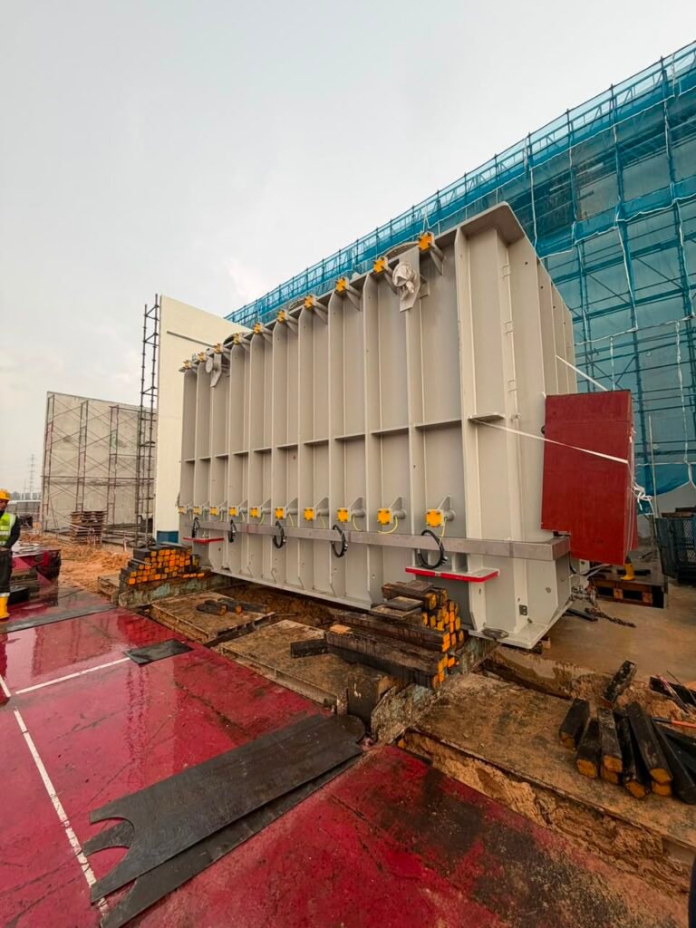 Side view of a large transformer supported during controlled movement towards its final position.